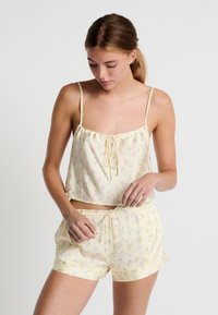 Conjunto de pijama amarillo claro con patrón de flores. La camiseta sin mangas tiene tirantes finos y un cordón; los pantalones cortos son elásticos con un diseño a juego.