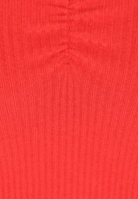 Rippstrickstoff in leuchtendem Rot, mit vertikalen Linien und einer strukturierten Oberfläche sowie einer Raffung in der Mitte.