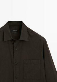 Dark brown button-up shirt with a classic collar, featuring a single chest pocket, smooth texture, and plastic buttons.