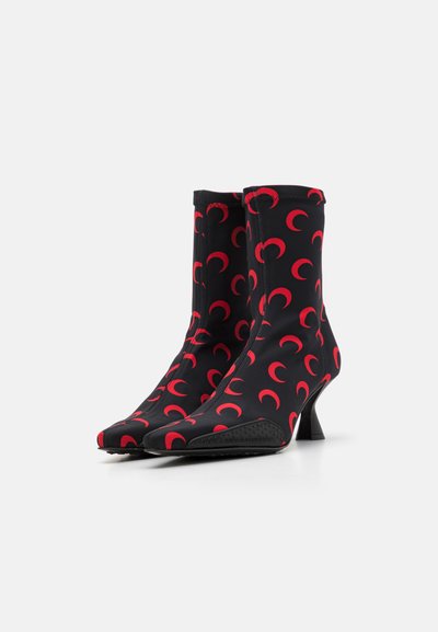 Botines negros con un diseño elegante, que presentan un patrón de luna creciente roja, puntera afilada y un tacón modesto. Fabricados en tela elástica.