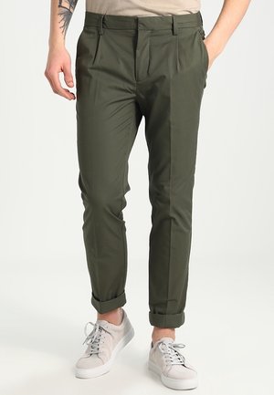 Olijfgroene broek van lichtgewicht stof met een tapered fit, voorzien van voorplooien en opgerolde mouwen, gecombineerd met grijze sneakers.