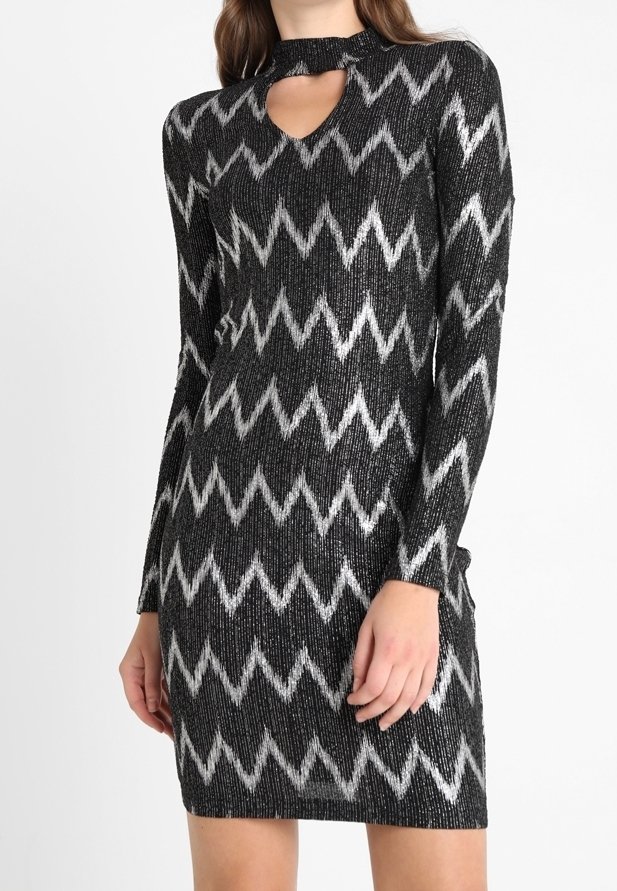 Robe longue à manches longues noire et argentée à motif zigzag avec une découpe en forme de serrure à l'encolure, portée par une personne debout.