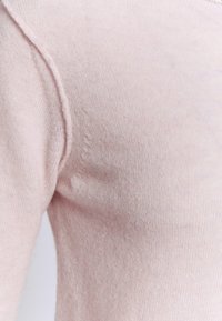Gros plan d'un tissu tricoté rose clair doux montrant la couture d'épaule et une texture lisse.
