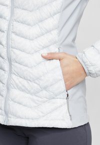 Jasnoniebieska ocieplana kurtka z teksturowanym, wzorzystym przodem, gładkimi rękawami, kieszenią na zamek i elastycznymi mankietami.