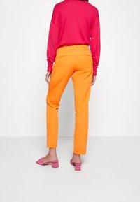 Jasno-pomarańczowe spodnie o dopasowanym kroju, połączone z długim różowym swetrem. Stylizacja zawiera delikatne tylne kieszenie oraz różowe mule na obcasie.