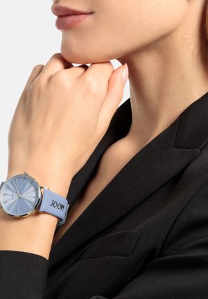 Helles blaues Lederarmbanduhr mit strukturiertem silbernem Zifferblatt, goldfarbener Hardware und dem Markenlogo "JOOP!" auffällig displayed.