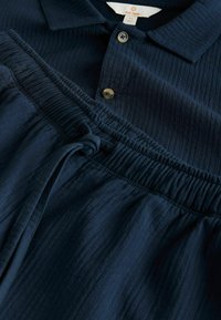 Tengerészkék polo ing bordázott textúrával, két gombbal és lazán illeszkedő derékpánttal, állítható húzózsinórral.