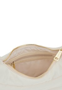 L'intérieur du sac en tissu beige présente une fermeture éclair dorée, une petite poche zippée et un revêtement textile lisse.