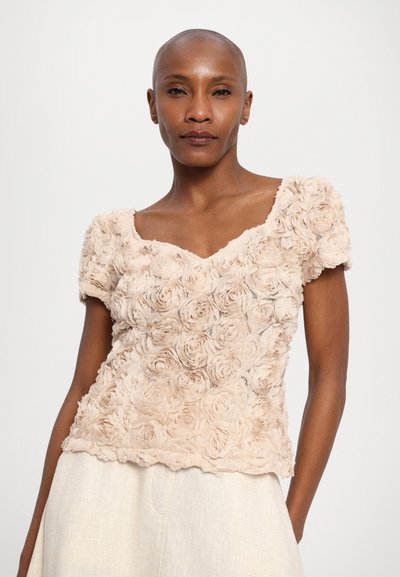 Beige blomsterbluse med teksturert stoff som har 3D rose mønstre, korte puffermuffer og V-hals design.