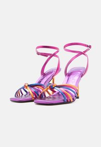 Ζευγάρι μεταλλιζέ μωβ πέδιλα με ψηλά τακούνια, πολύχρωμους πορτοκαλί και μπλε ιμάντες και λεπτούς λουρίδες στον αστράγαλο με αγκράφες.