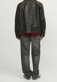 Chaqueta de cuero negra con un corte holgado, combinada con jeans de mezclilla gris con una textura desgastada y bolsillos estándar. Camisa de franela de cuadros rojos visible debajo.