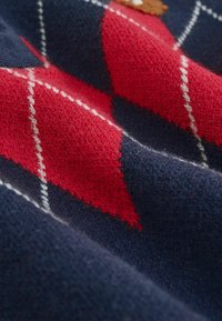 Gros plan sur un tissu bleu marine avec un motif en losanges argyle rouge et blanc et des détails en tricot texturé.