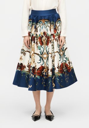 Midi spódnica w kwiatowy wzór z granatowym paskiem w talii i lamówką, noszona z białą bluzką i czarnymi balerinami z noskiem w szpic.