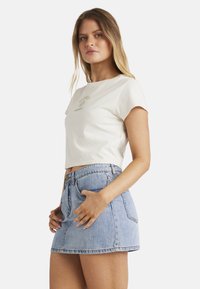 Hvid cropped t-shirt med et grønt logodesign, kombineret med en højtaljet lyseblå denimnederdel med knaplukning og lommer.