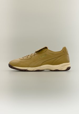 Ταμπά δερμάτινο αθλητικό παπούτσι με ταιριαστά κορδόνια, ανοιχτό μπεζ σόλα και επικάλυψη στην κορυφή, εμφανιζόμενο σε απλό φόντο.