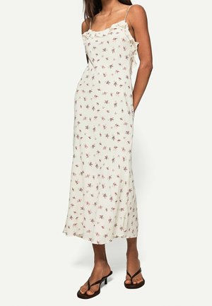 Robe midi fleurie crème avec fines bretelles et encolure à volants. Présente un motif subtil de fleurs roses et vertes, tissu doux et coupe décontractée.