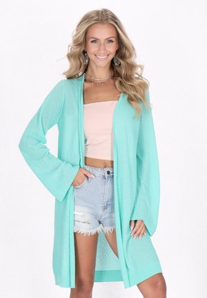 Cardigan leggero e strutturato in verde menta con maniche lunghe e svasate, dotato di una apertura frontale e un orlo posteriore leggermente più lungo.