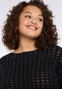 Černý pletený svetr s texturovaným, otevřeným vzorem tkaní, krátkými rukávy a širokým výstřihem, vyrobený z měkkého a prodyšného materiálu.