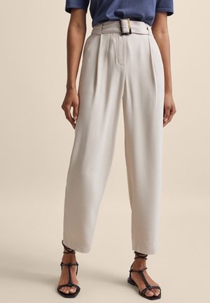 High-waist beige wide-leg trousers with belt buckle, worn with black strappy sandals and a tucked-in blue short-sleeve top.