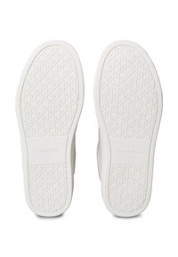 Beli podplati čevljev z reliefnim oprijemom, ki vsebuje ponavljajoč se vzorec črke "C" in vtisnjeno blagovno znamko "Calvin Klein" blizu območja pete.