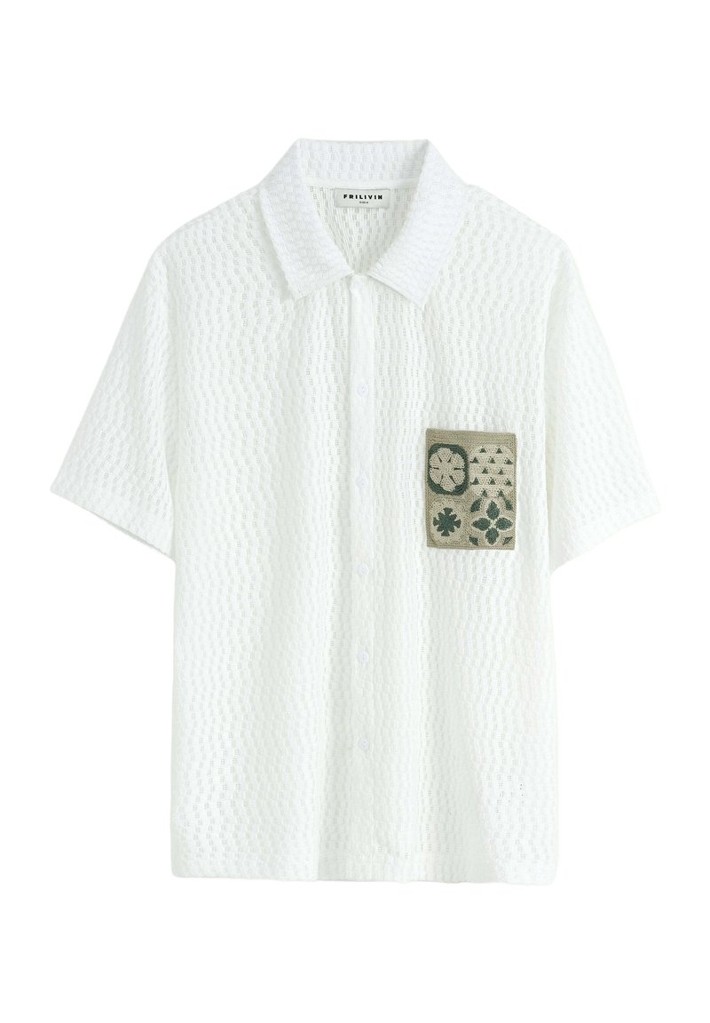 Chemise blanche à manches courtes avec un motif texturé, présentant une poche plaquée verte avec des motifs floraux et géométriques. Fermeture à boutons sur le devant.