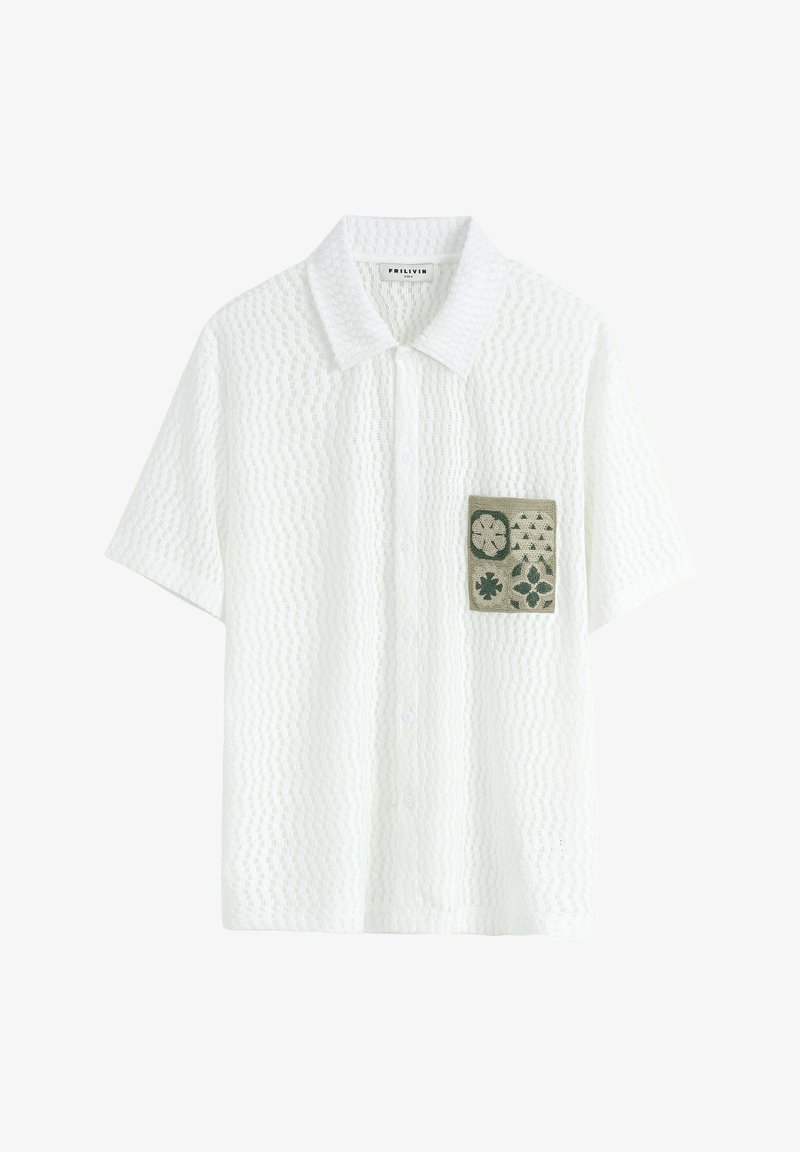 Chemise blanche à manches courtes avec un motif texturé, présentant une poche plaquée verte avec des motifs floraux et géométriques. Fermeture à boutons sur le devant.