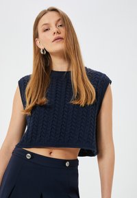 Marinblå kort stickad topp med texturerad kabelmönster, breda ärmhål och ribbad nederkant. Matchas med skräddarsydda marinblå höga byxor.