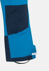 Zilā un tumši zilā patchwork slēpošanas bikses, ar elegantu dizainu, gludu tekstūru, elastīgu aproci un atstarojošu akcentu apakšmalā.