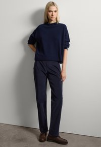 Un pull en maille bleu marine avec un col haut, associé à un pantalon en velours côtelé bleu marine et des chaussures en cuir marron. Texture lisse avec une coupe décontractée.
