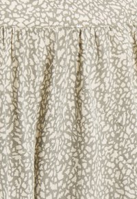 Tecido com uma base bege clara e um padrão abstrato cinza texturizado, apresentando detalhes franzidos ao longo da borda superior.