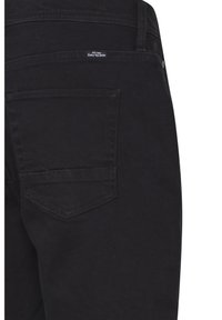 Sorte denimbukser med en enkelt baglomme og en buet sømdetalje. Stofoverfladen er glat med en let tekstur.