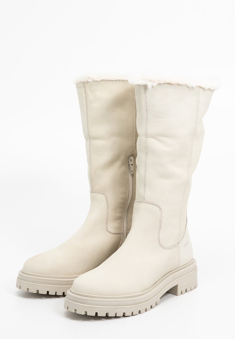 Bottes en cuir beige montantes avec une doublure en fourrure douce en haut, dotées d'une fermeture éclair sur le côté et d'une semelle rugueuse et texturée.