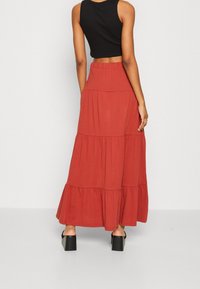 Jupe maxi tiered couleur rouille en tissu doux avec une taille élastique, associée à un crop top noir ajusté et des talons épais.
