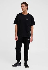 Svart t-shirt och joggingset i mjukt tyg. T-shirten har en liten vit logga på bröstet; joggingbyxorna har en avslappnad passform och mudd.