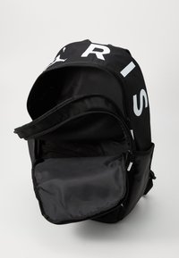 Black backpack with large white lettering on the top, featuring a zippered main compartment and a smooth, durable fabric texture.