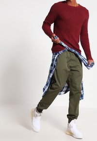 Punainen neule, oliivinvihreät housut ja valkoiset lenkkarit. Sininen ruudullinen paita sidottuna vyötärölle. Rentoa, kerroksellista asua, jossa on erikoiset tekstuurit.