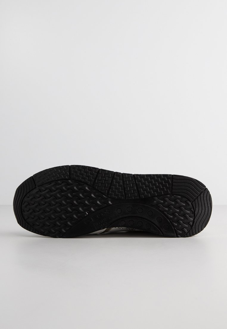 Suela de zapato de goma negra con patrones de textura antideslizantes y agujeros de aire circulares, con un talón ligeramente curvado y un diseño de relieve prominente.