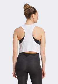 Top court blanc avec un dos nageur, associé à un legging noir taille haute. Tissu lisse, détails minimalistes et silhouette ajustée.