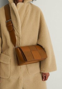 Bolso de hombro de piel marrón con un diseño acolchado, que presenta una textura suave y paneles en contraste. Correa ajustable.