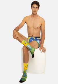 Caleçons boxers colorés avec un motif bleu et jaune de soleil et d'océan, associés à des chaussettes montantes présentant des designs tropicaux vibrants.