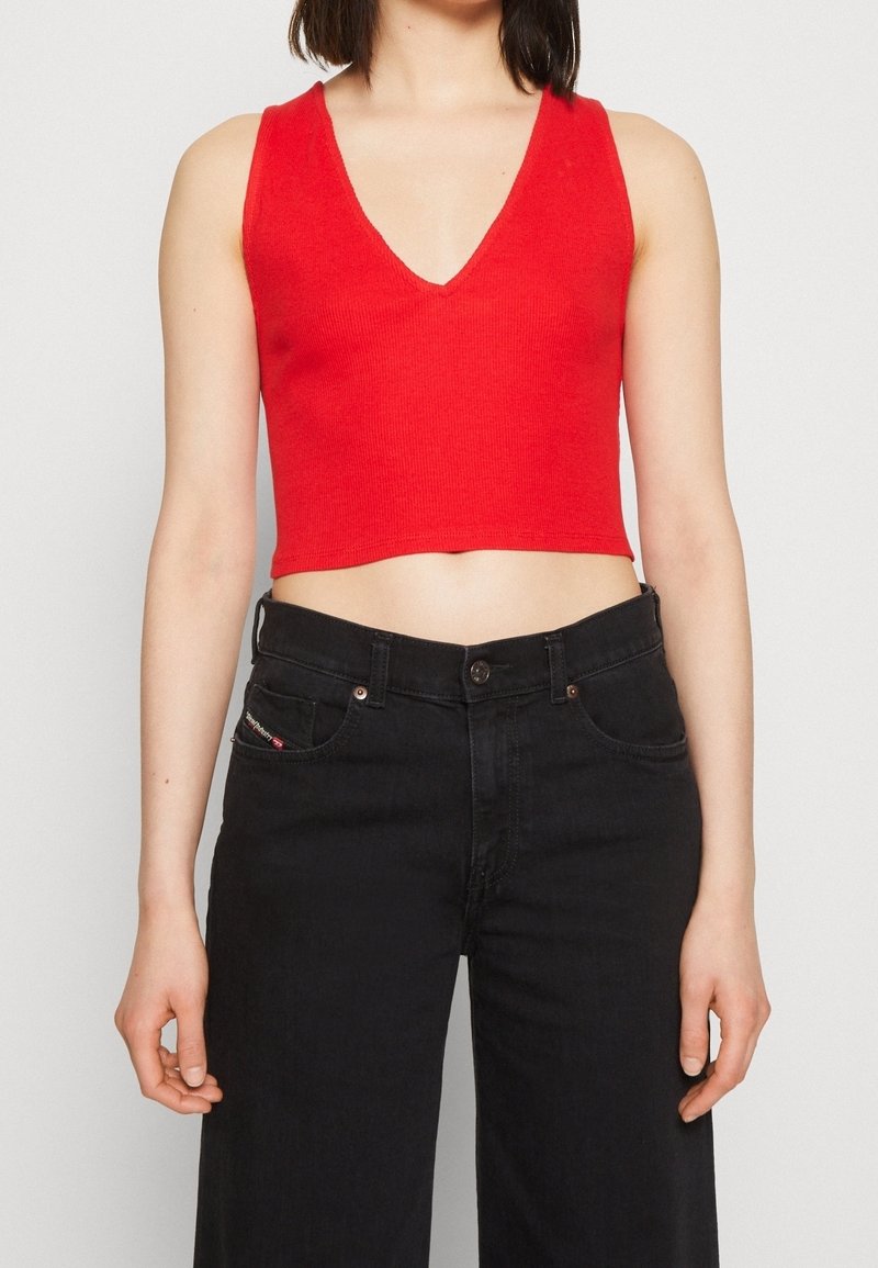 Haut court rouge à côtes avec un décolleté en V profond, associé à un jean noir taille haute avec fermeture à bouton et poches latérales.