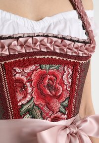 Corsage en tissu rouge riche, broderie florale complexe et accents décoratifs en satin avec un ruban rose noué à la taille.