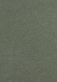 Tissu côtelé vert foncé avec une texture douce, présentant des lignes verticales. Le matériau semble extensible et léger.