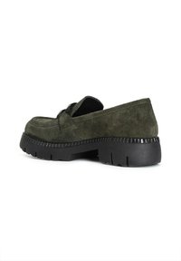 Mocassino in suede verde scuro con suola in gomma nera leggermente sollevata. Presenta una tomaia cucita e una fascia decorativa sul davanti.
