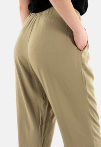 Pantaloni larghi di colore verde chiaro, con vita elastica e tasche laterali; texture morbida con un sottile dettaglio di drappeggio.