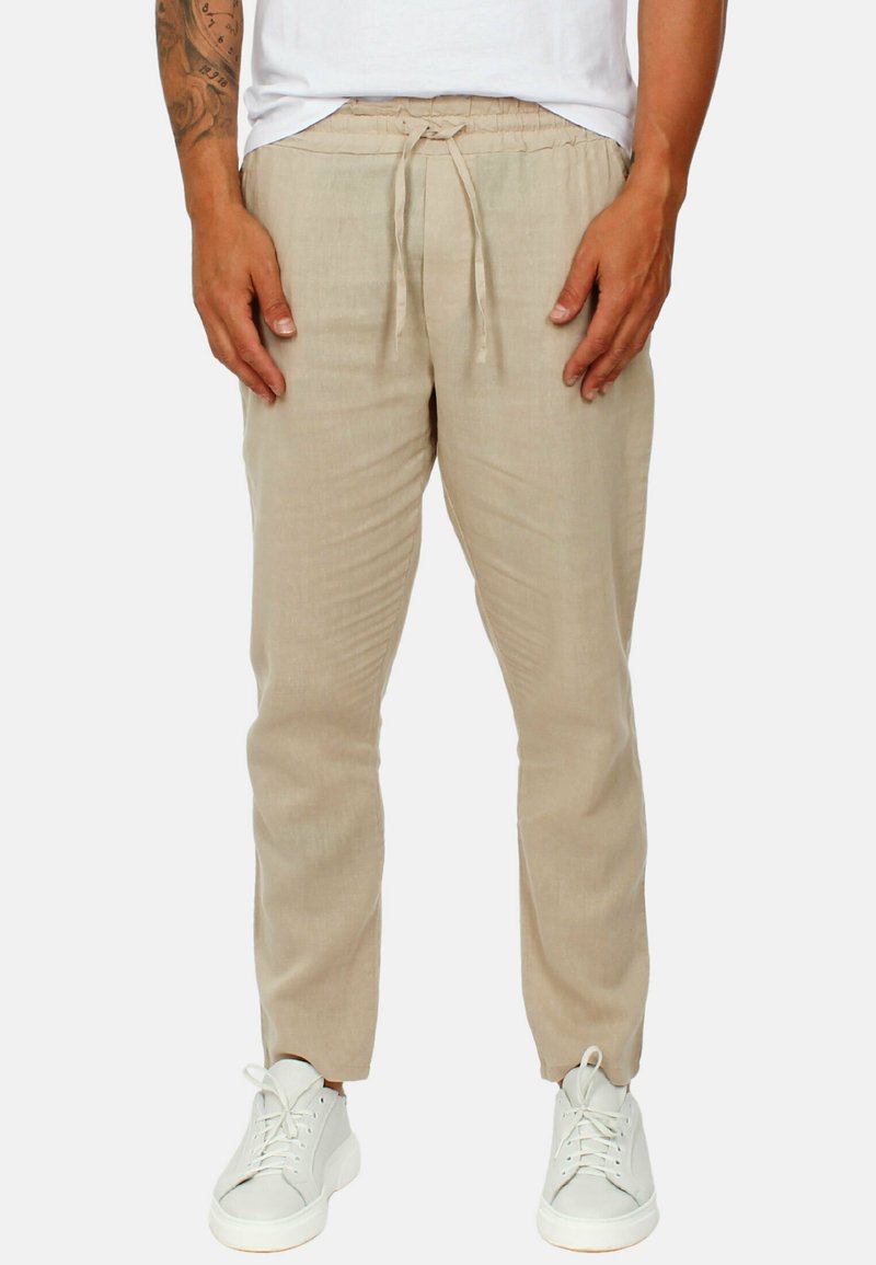pantaloni in lino leggeri beige con vita regolabile, gambe affusolate e una texture morbida, abbinati a sneakers bianche.
