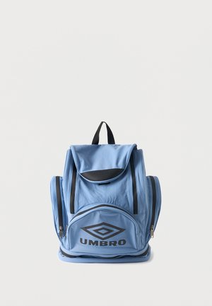 Sac à dos Umbro bleu clair avec plusieurs compartiments zippés et une poignée supérieure sur fond gris uni.