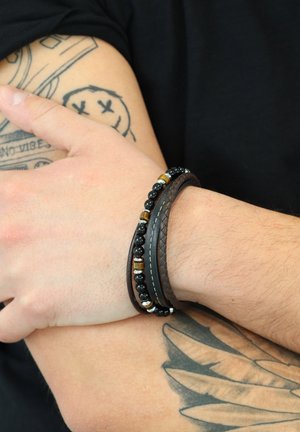 Leather and bead bracelet featuring black stones, metal accents, and woven texture. Worn on a wrist, contrasting with skin tone and tattoo.