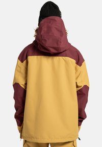 Wasserabweisende Jacke mit einem Farbblockdesign in Senfgelb, Burgunderrot und Braun. Sie hat eine Kapuze und elastische Bündchen.