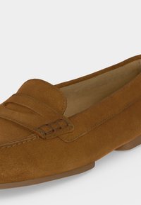 Καφέ μοκασίνι από σουέτ με χαμηλό τακούνι, ραμμένη μύτη και λουράκι στο πάνω μέρος.